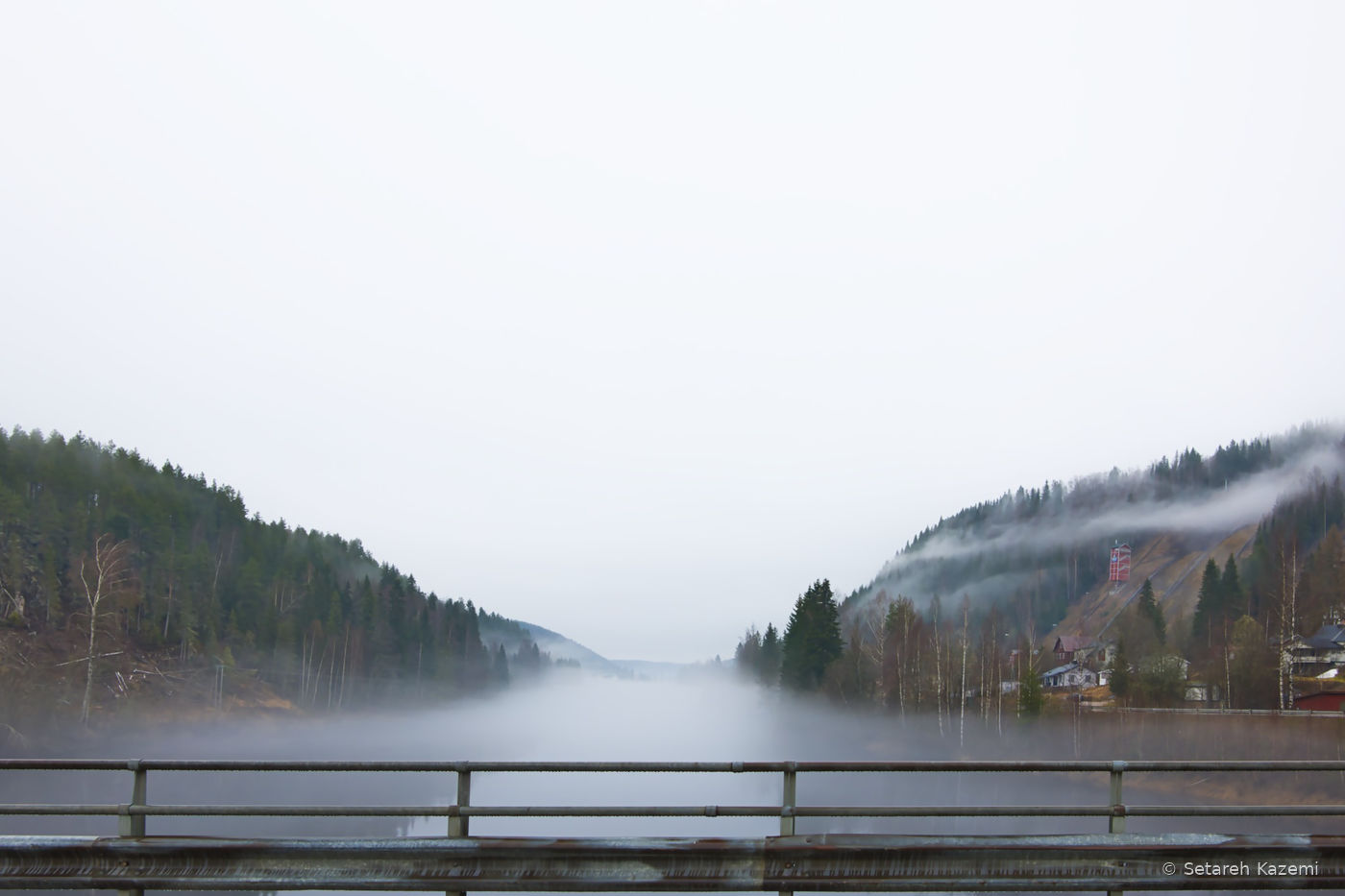 Fog stretching across a river valley beyond a bridge railing.